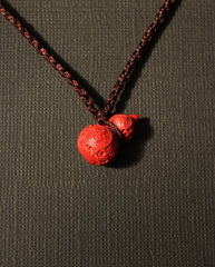 Carved Hulu cinnabar necklace on dark background