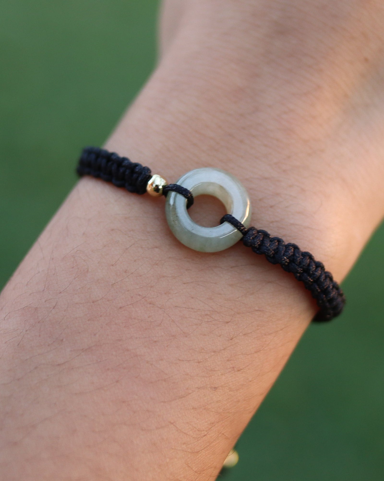 A close-up of a person's wrist wearing a black braided cord bracelet with a circular light gray stone centerpiece and a small gold accent.