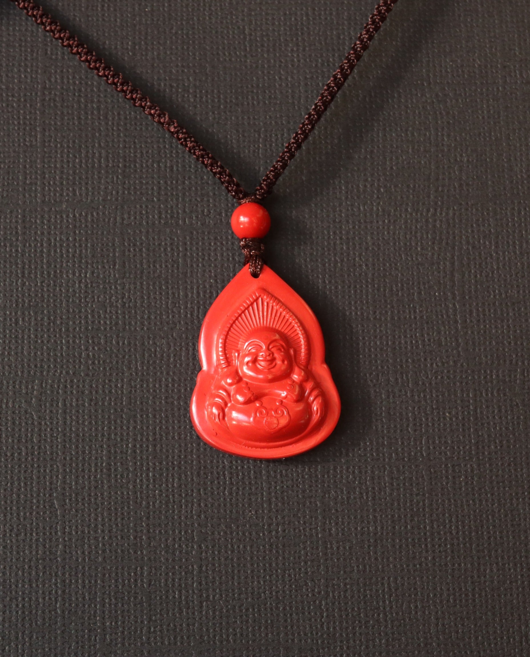 Seated Laughing Buddha cinnabar necklace on dark background