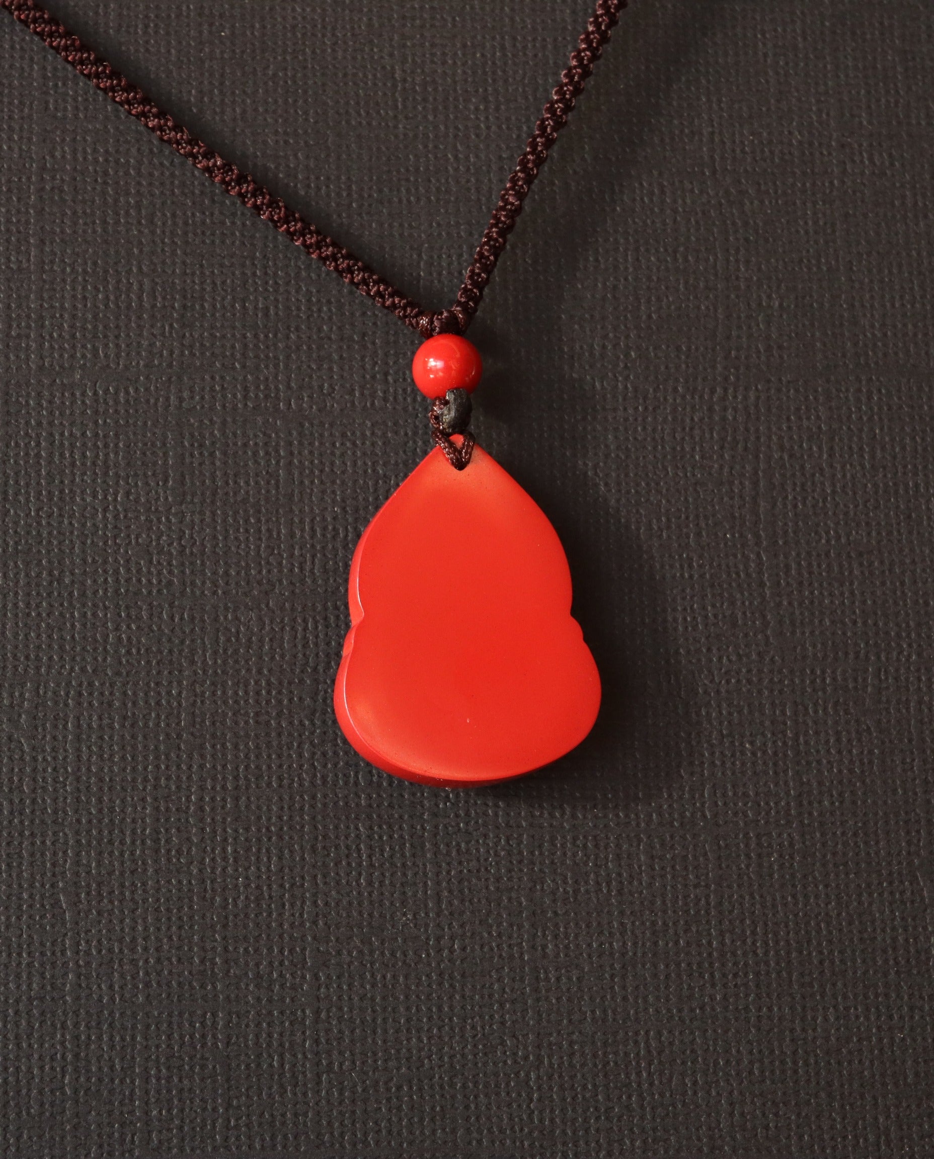 Seated Laughing Buddha cinnabar necklace on dark background