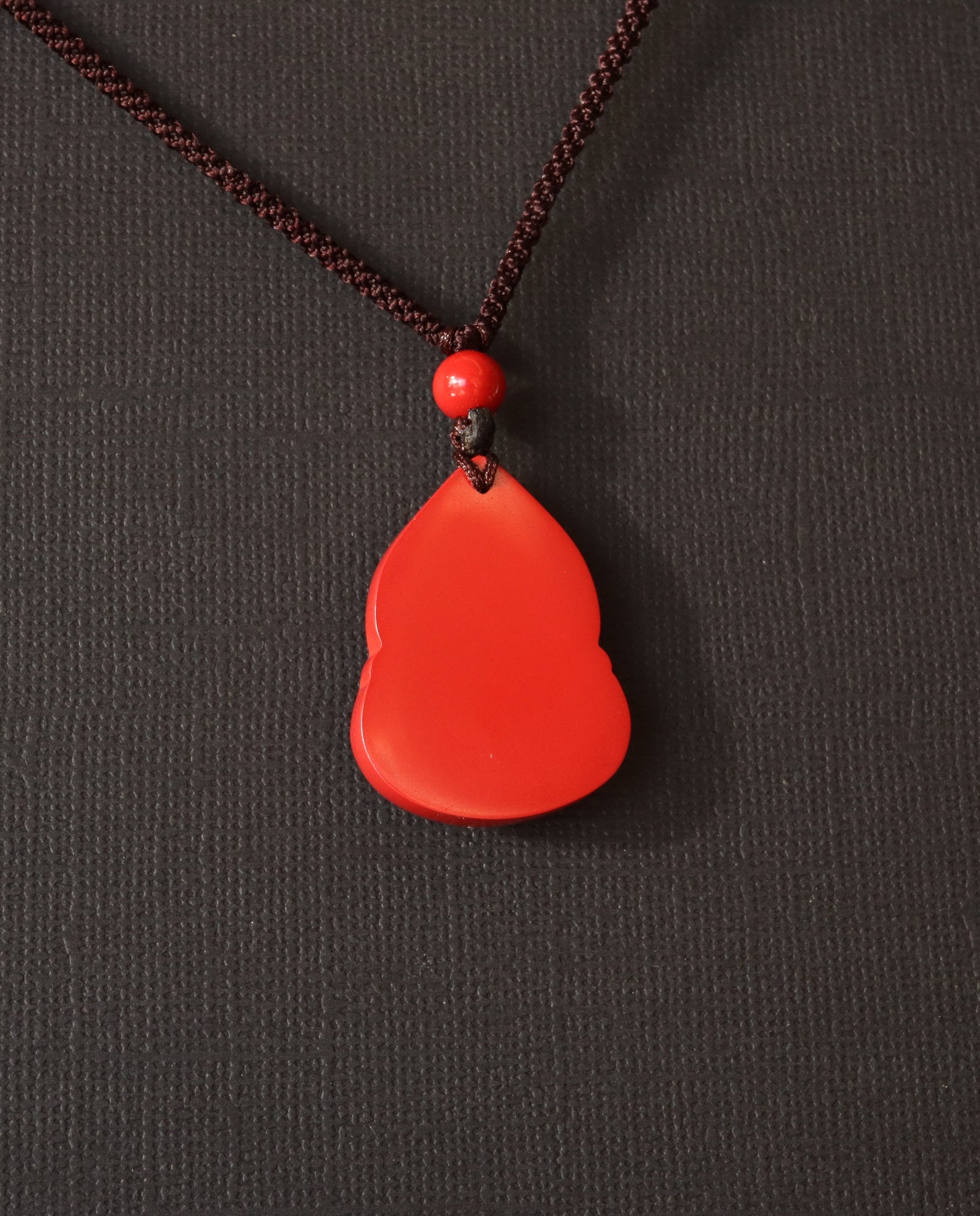 Seated Laughing Buddha cinnabar necklace on dark background