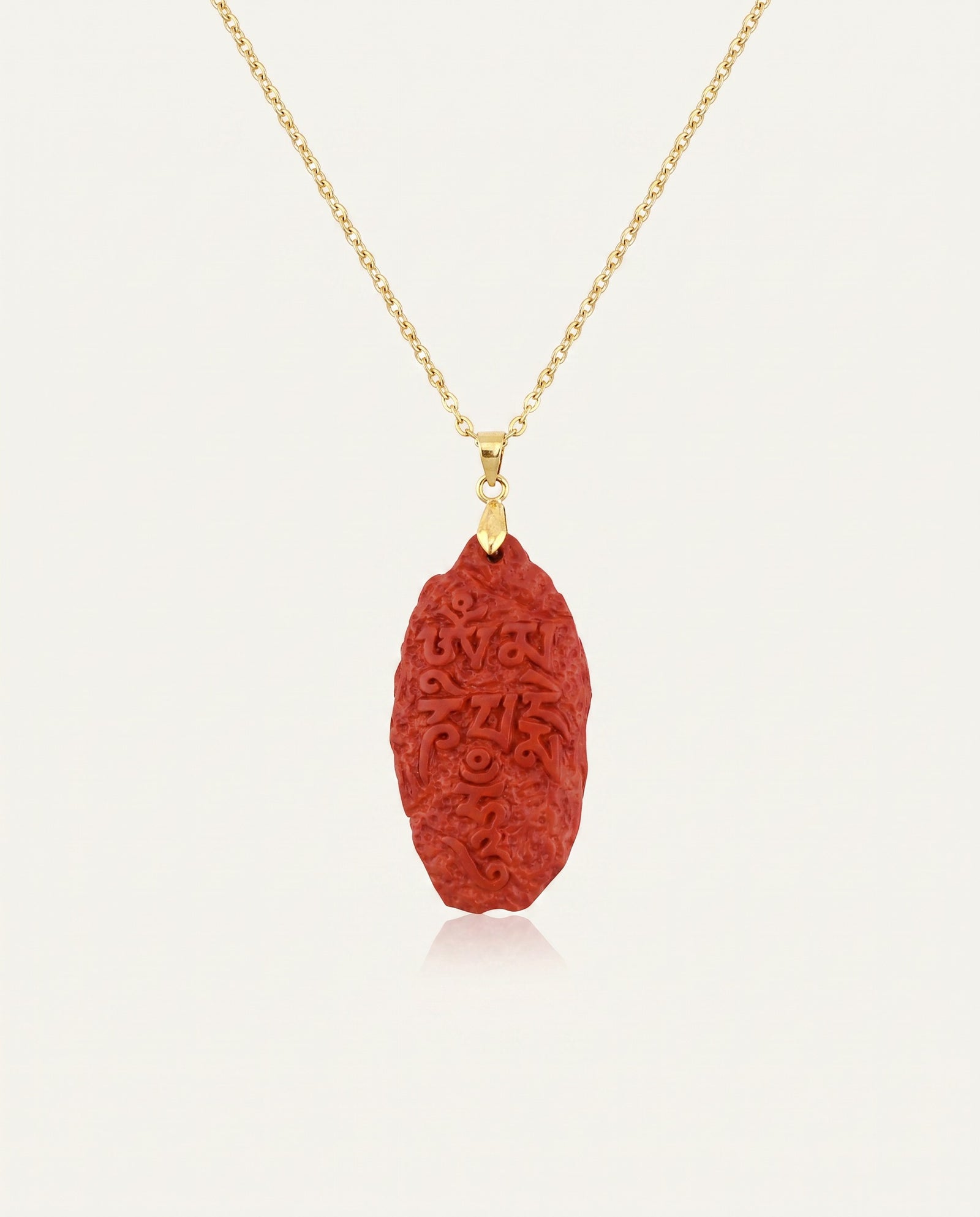 Six Character Mantra cinnabar necklace on gold chain, ivory studio background